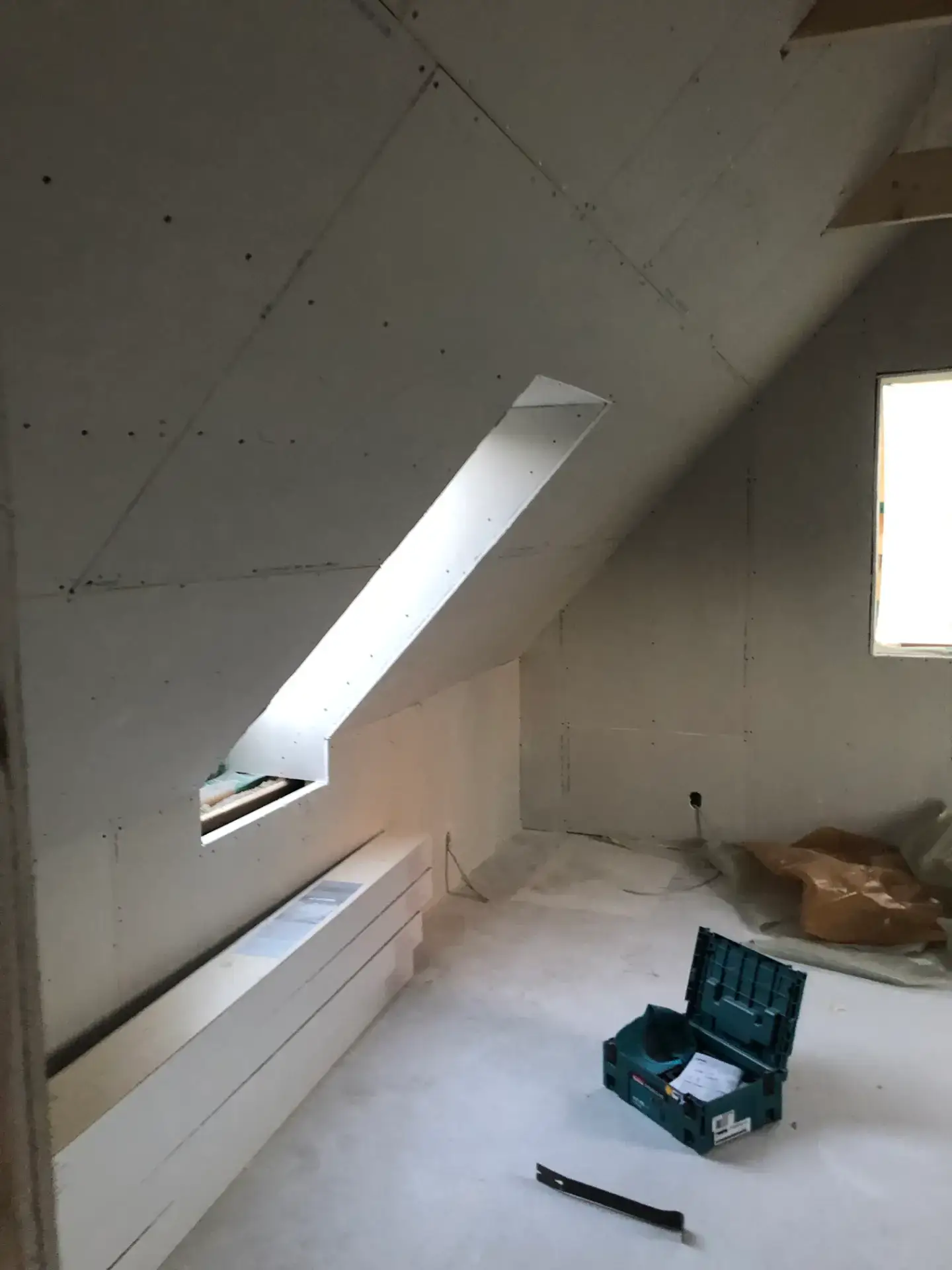 Indendørs byggeplads med skrå væg og vinduer under installation.