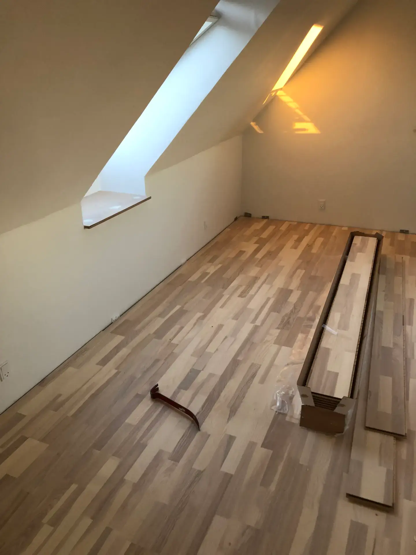 Nyrenoveret loftsrum med skråvindue og trægulv under installation.