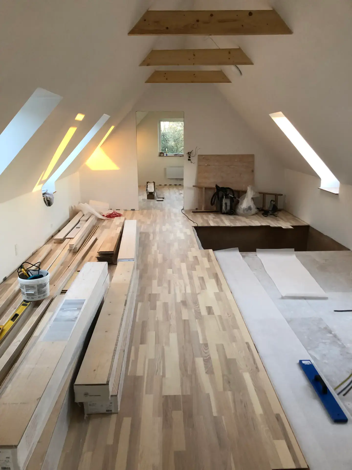 Indretning af et loftsrum med tagvinduer og træbjælker under renovering.