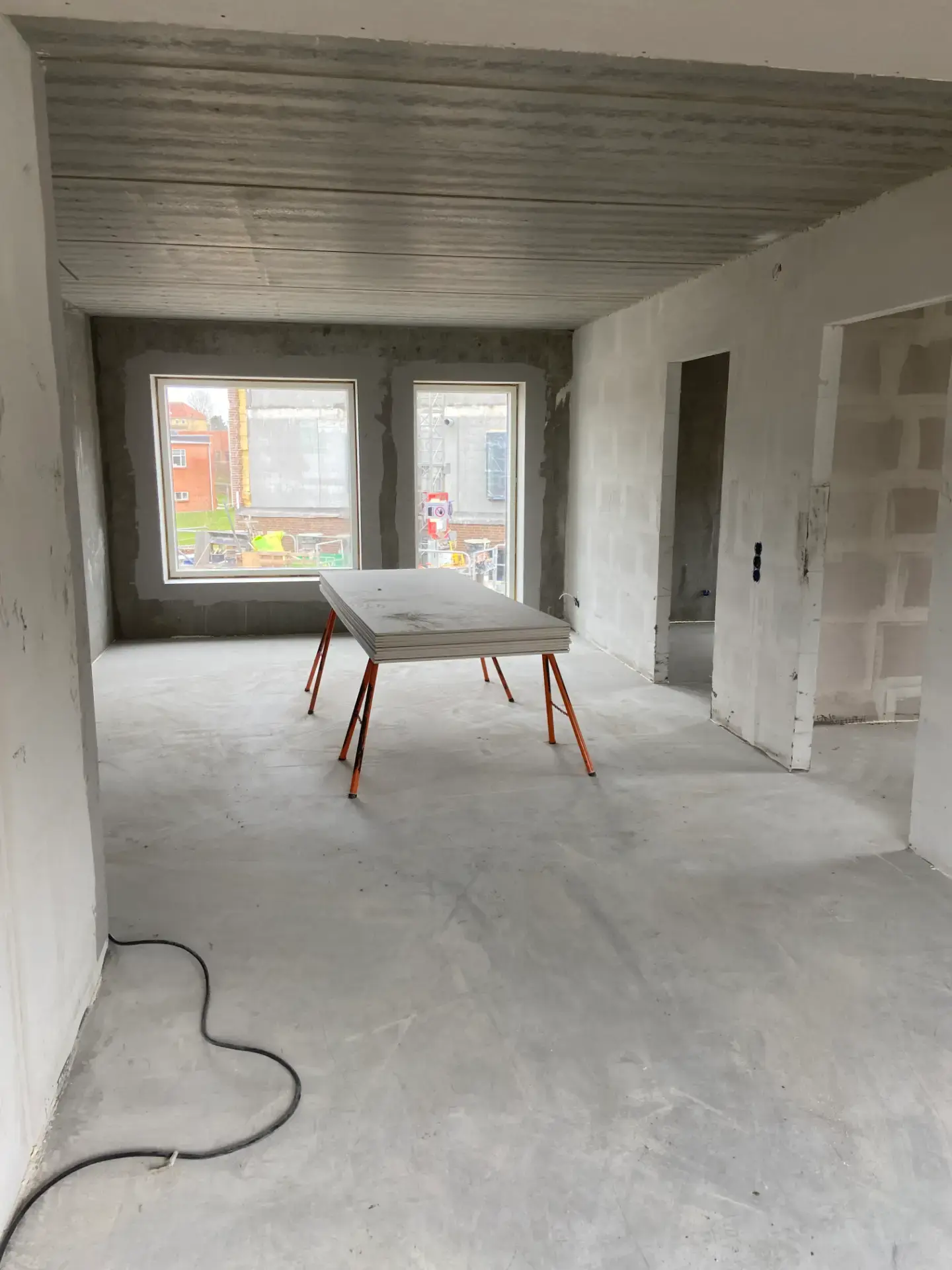 Indendørs byggeplads med rå vægge og store vinduer.